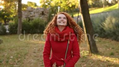 一个快乐的红头女人在秋天的一天里到处扔<strong>树叶</strong>，抬头看。 秋天的<strong>树叶飘落</strong>